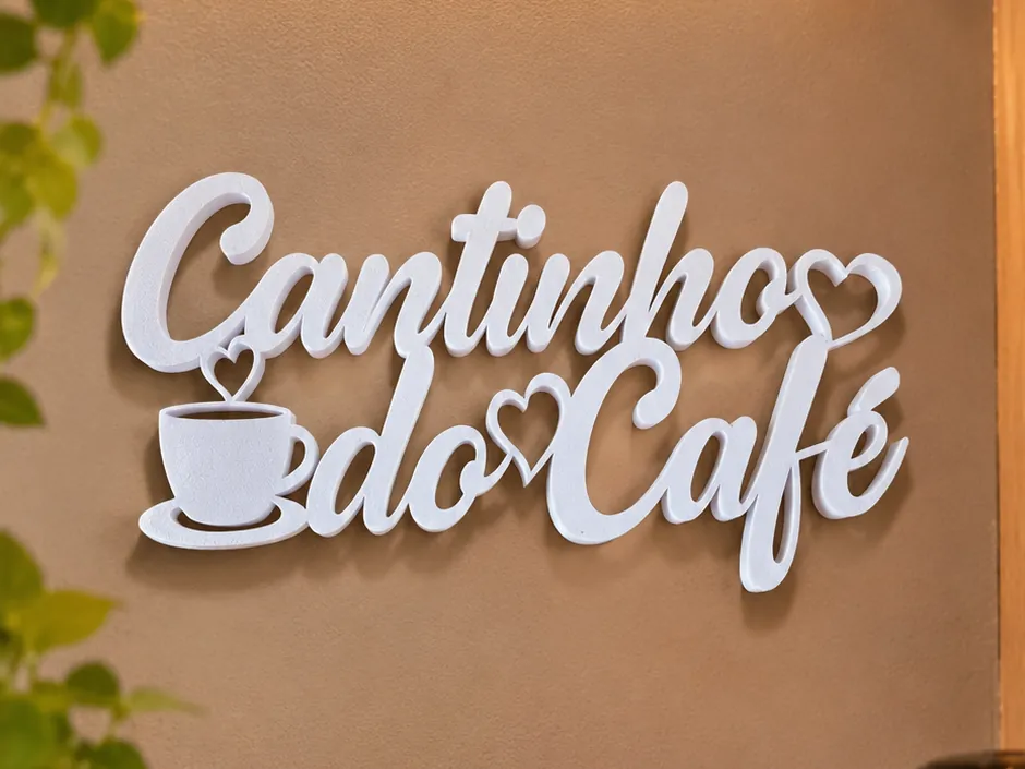 Placa de parede branca em letra cursiva, Cantinho do Café, com uma xícara e corações, presa numa parede marrom acima do café